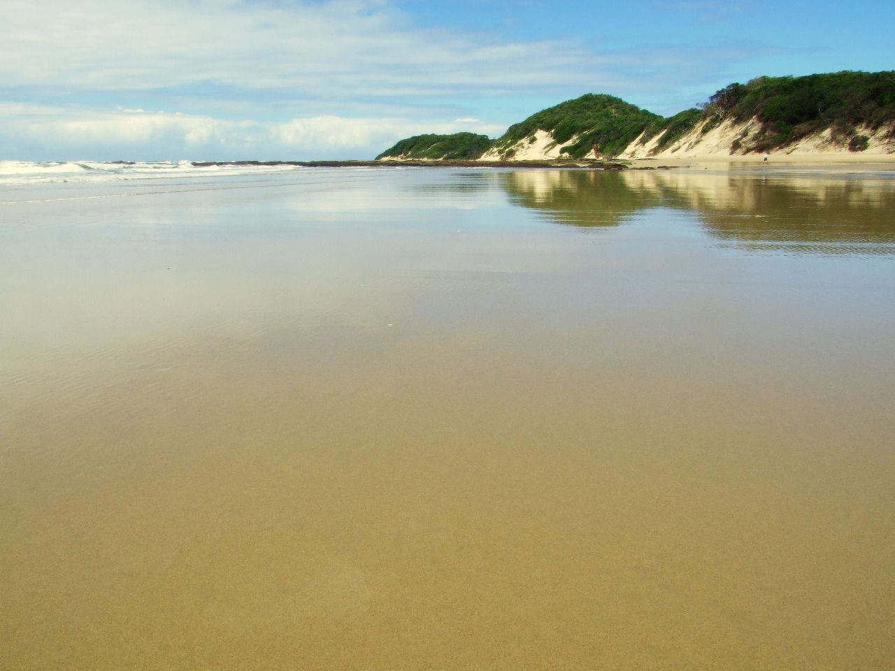 Wet sand reflecting the dunes and sky at low tide