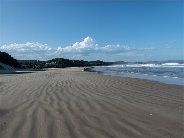 Empty beach with rippled sand running towards the headland