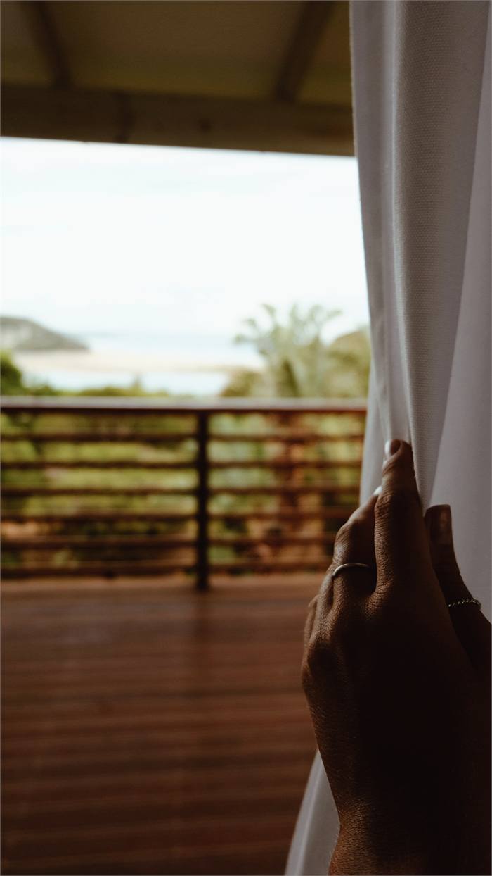 A curtain drawn back from a tree house doorway onto a deck with the sea beyond