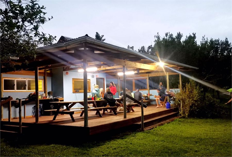 The camping boma lit up at dusk with the deck and tables under a thatched roof