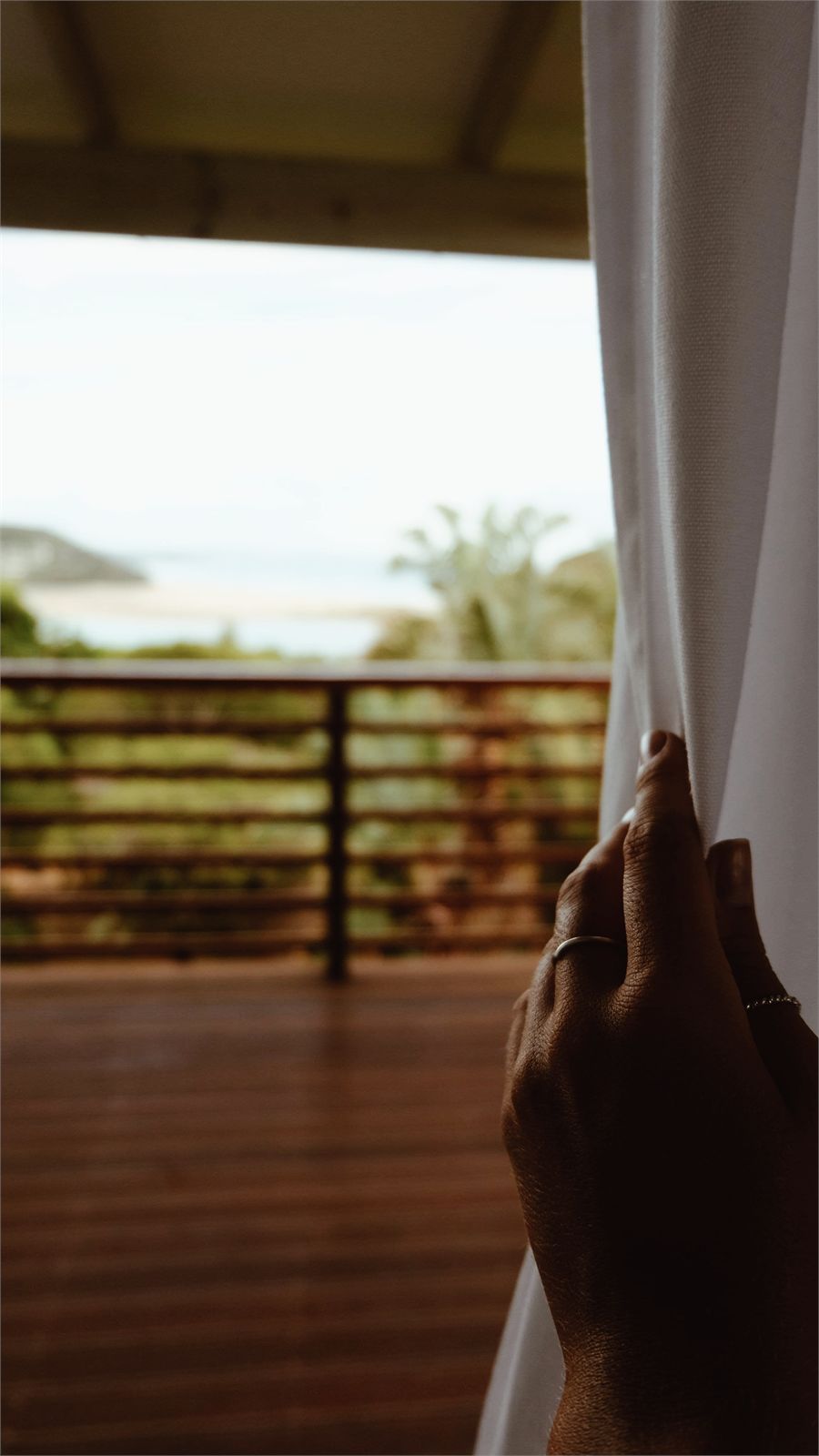 A curtain drawn back from a tree house doorway onto a wooden deck with the sea beyond